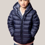 Child wearing a blue puffer jacket and white beanie on a beige background